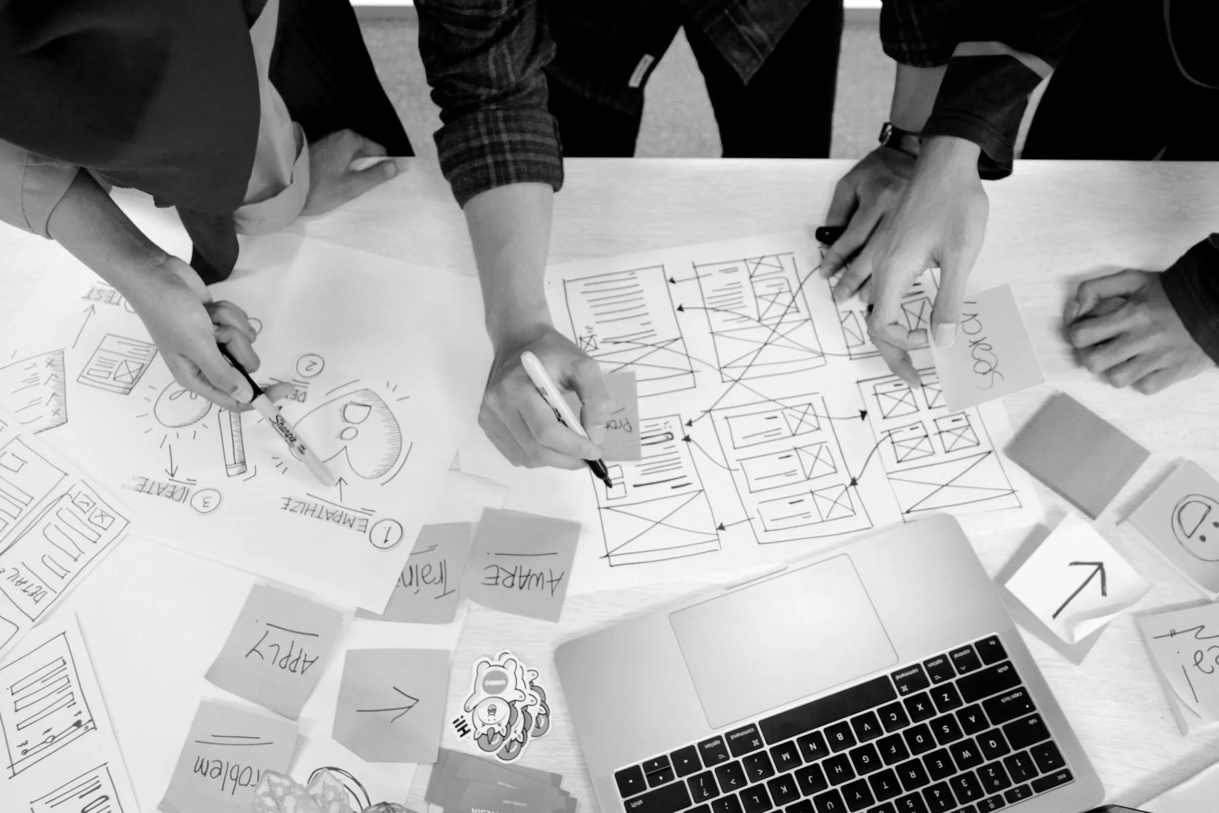 Designers sketching wireframes on paper next to a laptop and phone